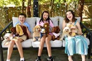 Three laughing kids on a garden sofa covered in teacup poodles